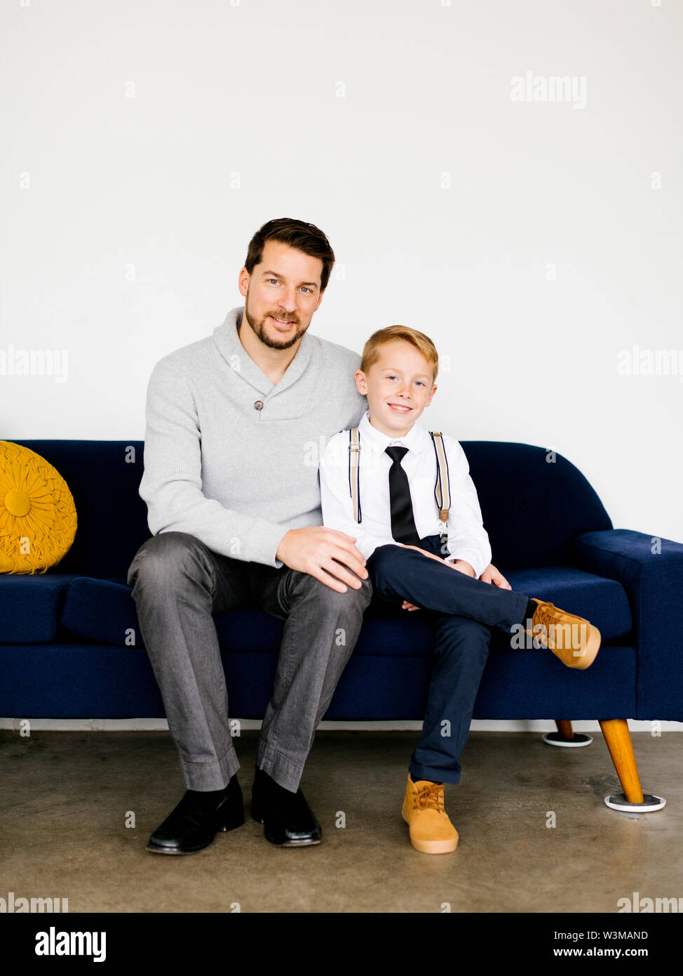 Smiling father and son sitting on sofa Stock Photo