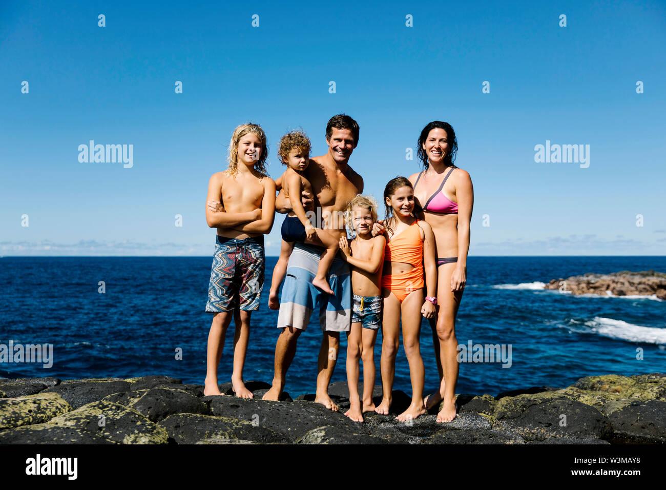 Smiling family standing on rocks by sea Stock Photo