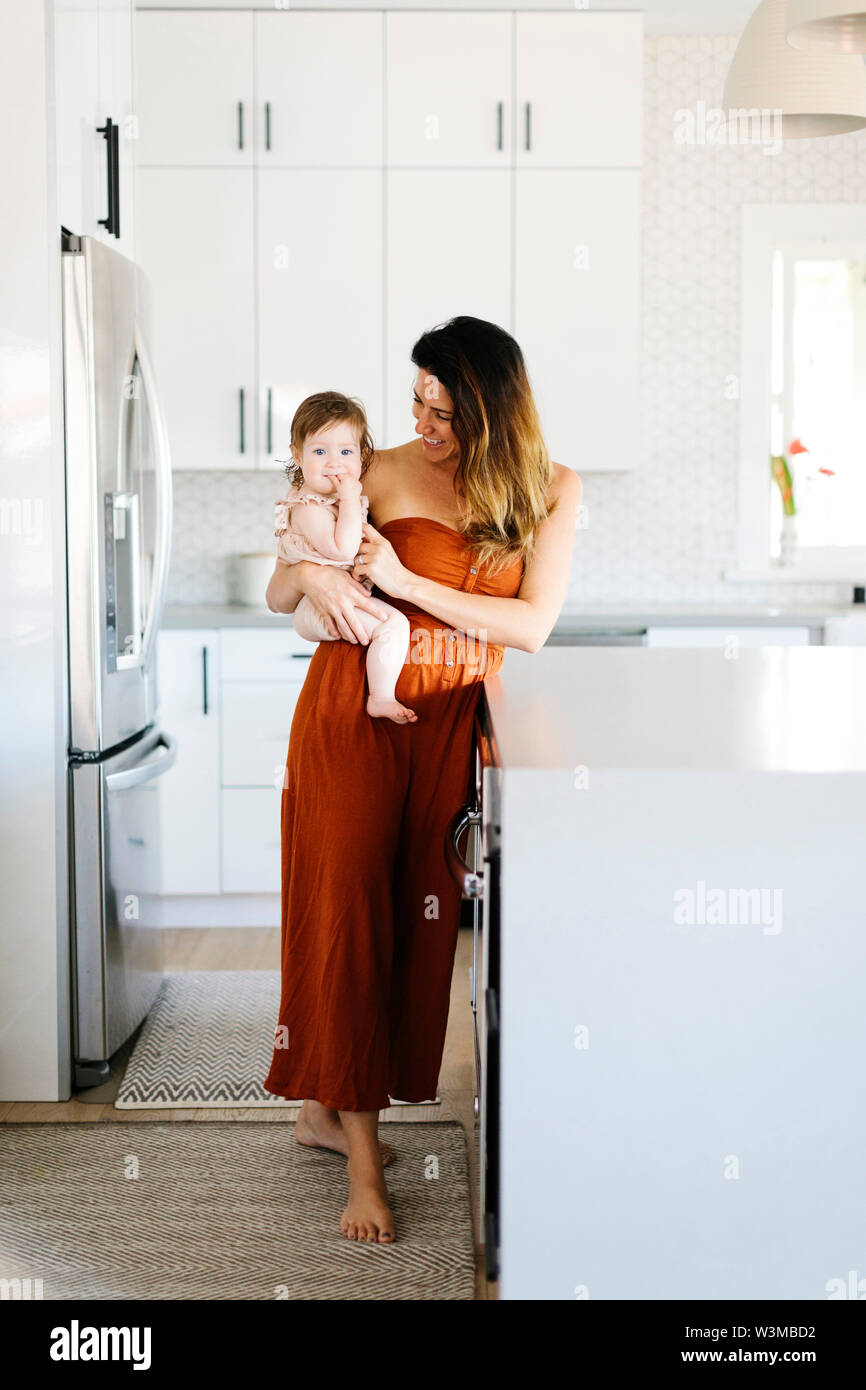 Woman carrying her baby daughter in kitchen Stock Photo