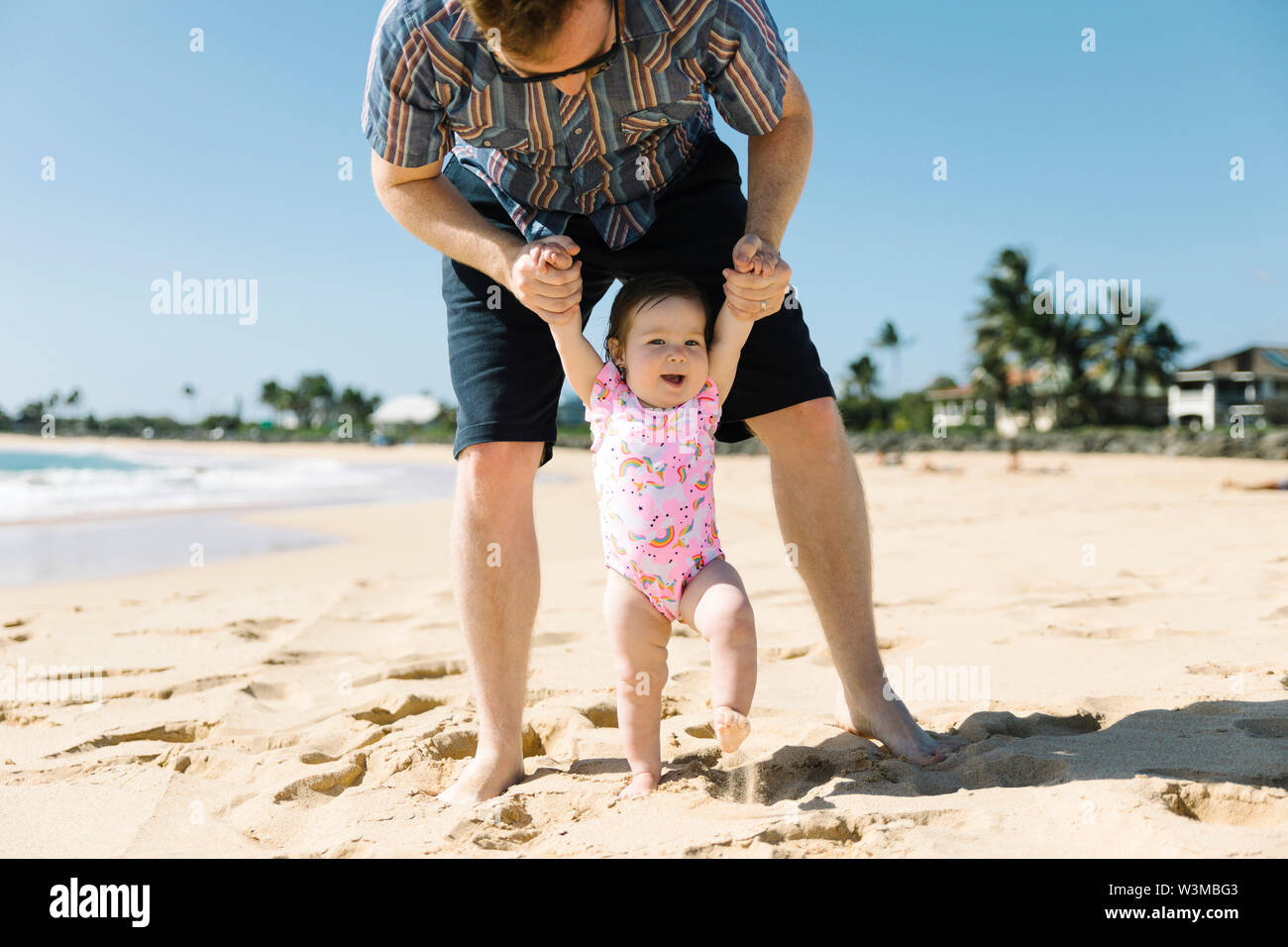 Father helping his baby girl walk on beach Stock Photo