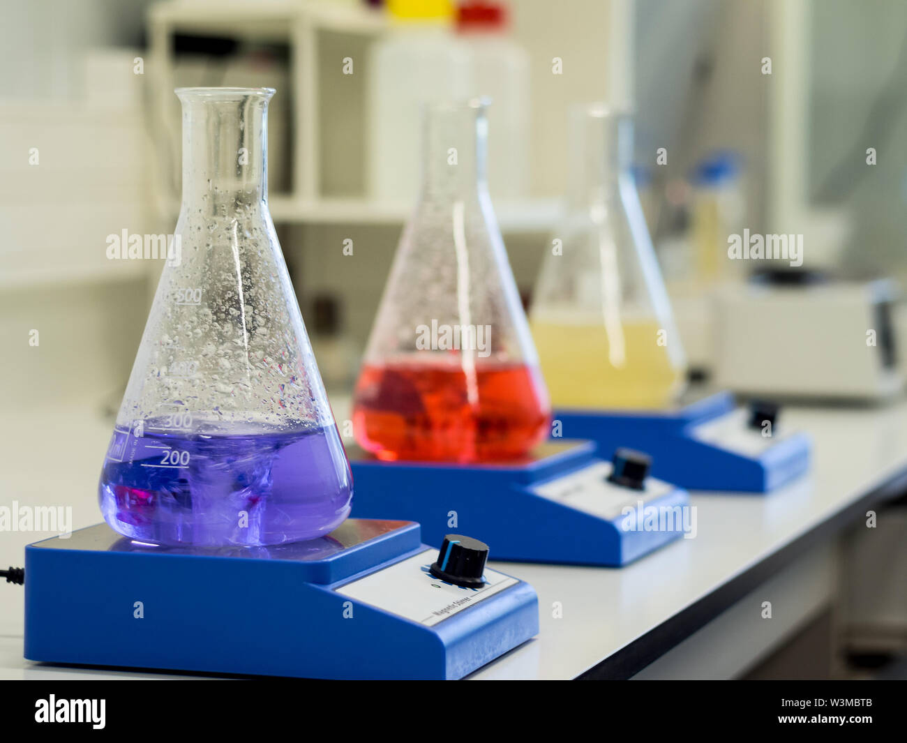 Erlenmeyer flasks with colorful solutions on a magnetic stirrer in a lab Stock Photo