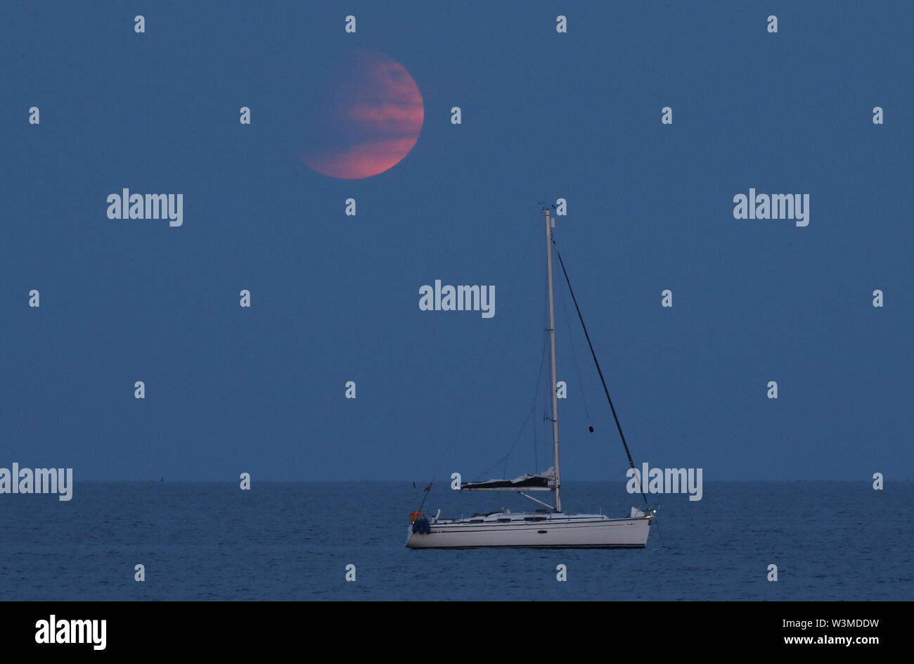 A partial lunar eclipse is visible above rises over a boat moored off ...