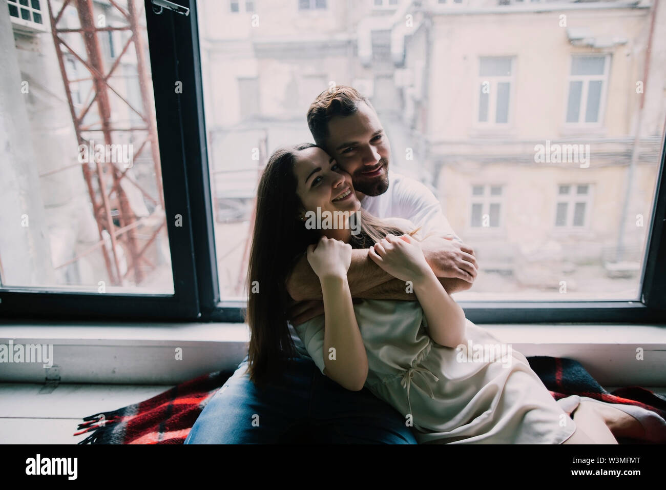 Young couple embracing by apartment window Stock Photo