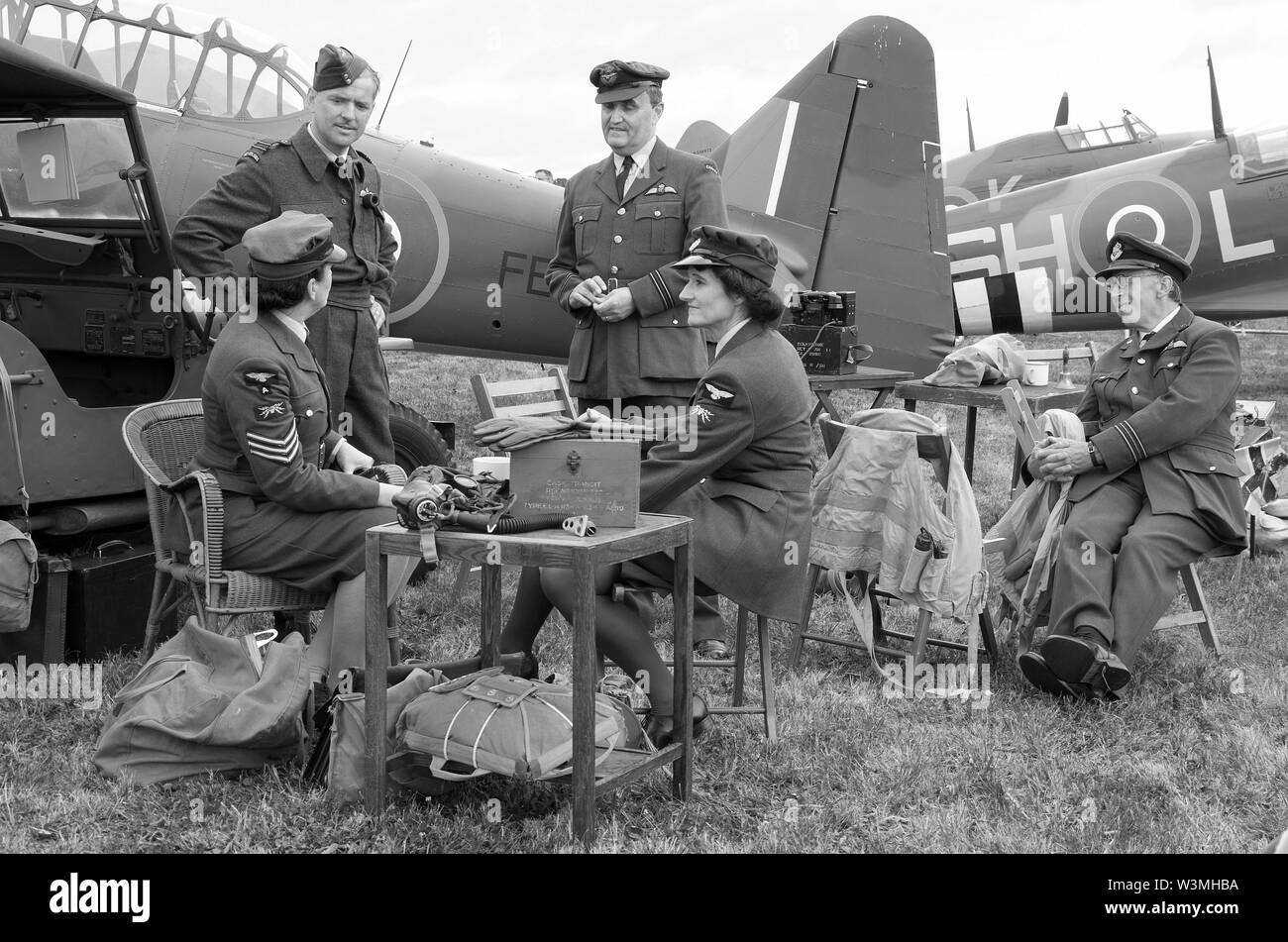 Battle of Britain era Second World War scenario with pilots, WRAFs & ground crew engineer re-enactors in discussion. Planes. Monochrome. Black & white Stock Photo