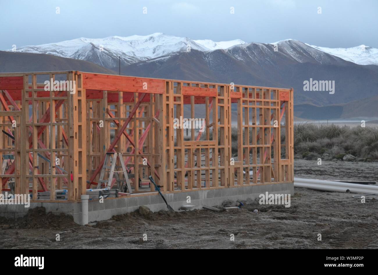 Wooden frame of a residential house under construction in the winter with frost on the ground and snow capped peaks in the background Stock Photo