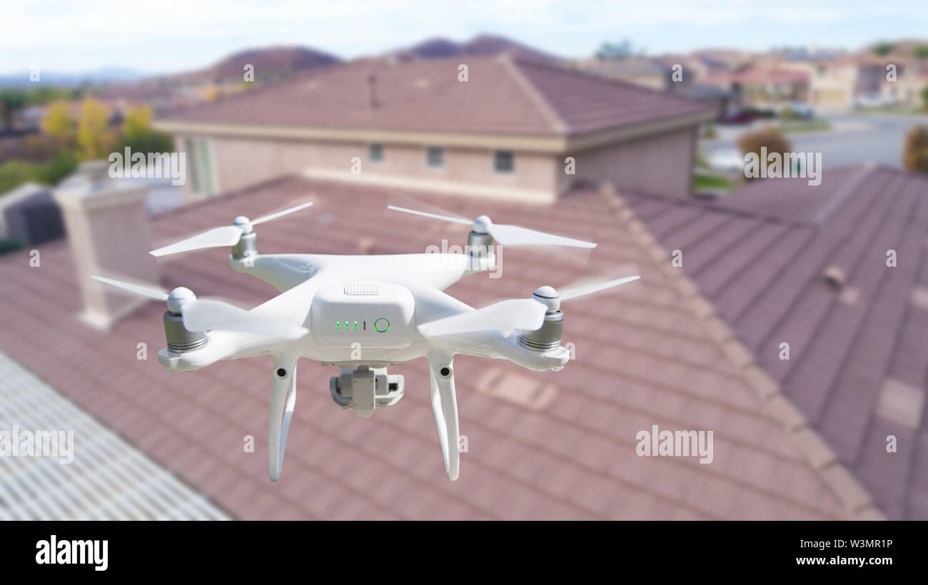 Unmanned Aircraft System (UAV) Quadcopter Drone In The Air Over House Inspecting the Roof. Stock Photo