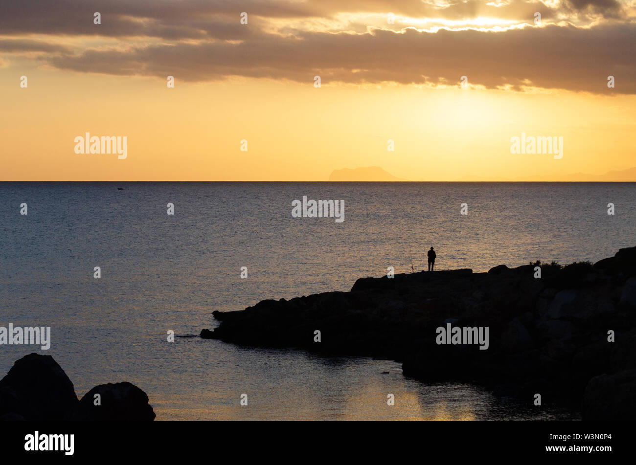 Al baño de un atardecer un hombre sale a pescar en una de las calas de Isla Plana. Stock Photo