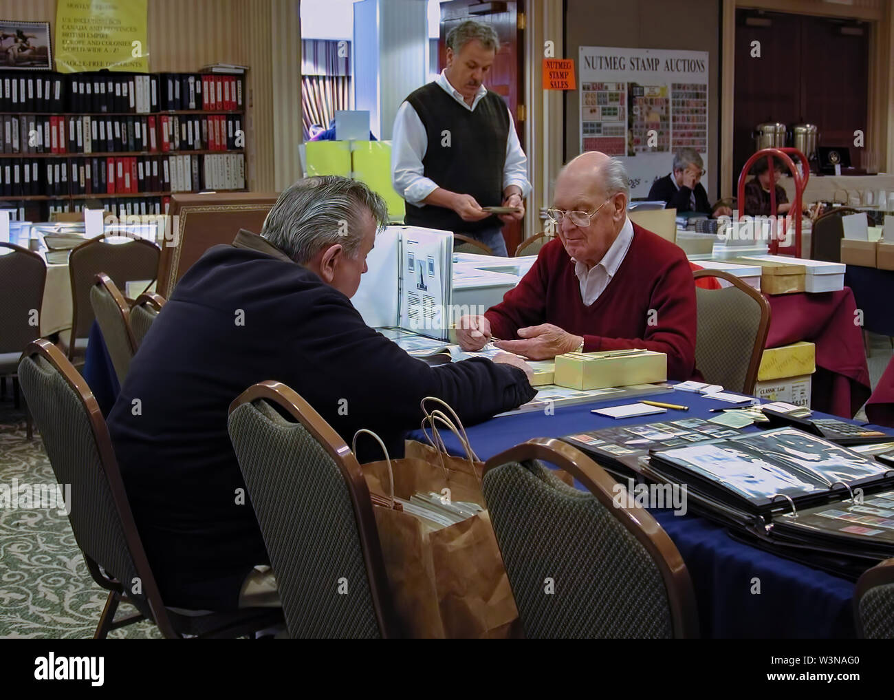 Cromwell, CT USA. Mar 2015. Two elderly men talking and dealing with each other on trades and purchases at a stamp auction event. Stock Photo