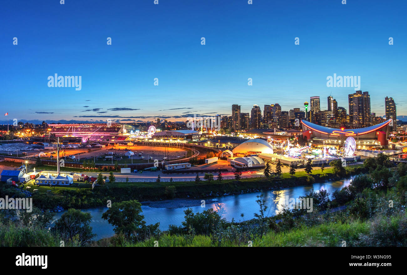 CALGARY, CANADA - JULY 14, 2019: Panorama of sunset blue hour over the Calgary Stampede fairgrounds surrounded by the Bow River with the city's urban Stock Photo