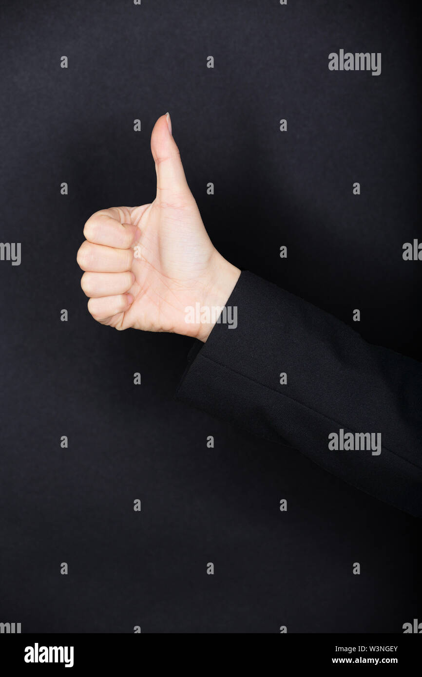 Person in dark clothing giving a Thumbs up gesture of approval and success against a dark studio background with copyspace. Black texture background.. Stock Photo