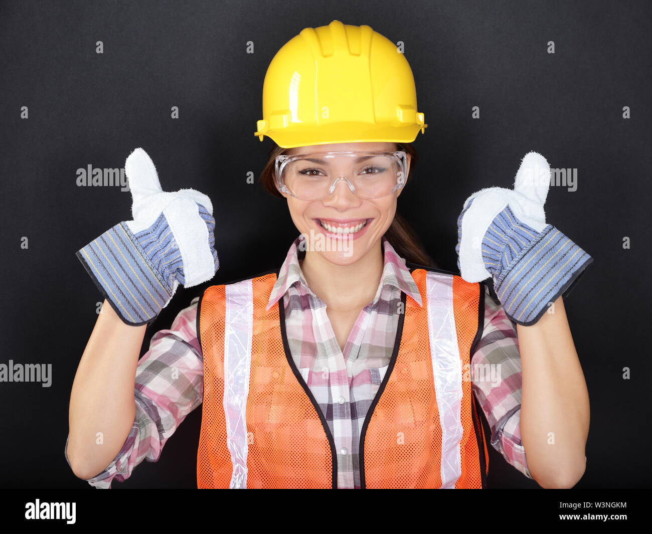 Construction worker happy woman doing thumbs up with protection wear. Young  woman wearing safety glasses, vest and yellow hard hat for security and  protection on black background. Asian female model Stock Photo -