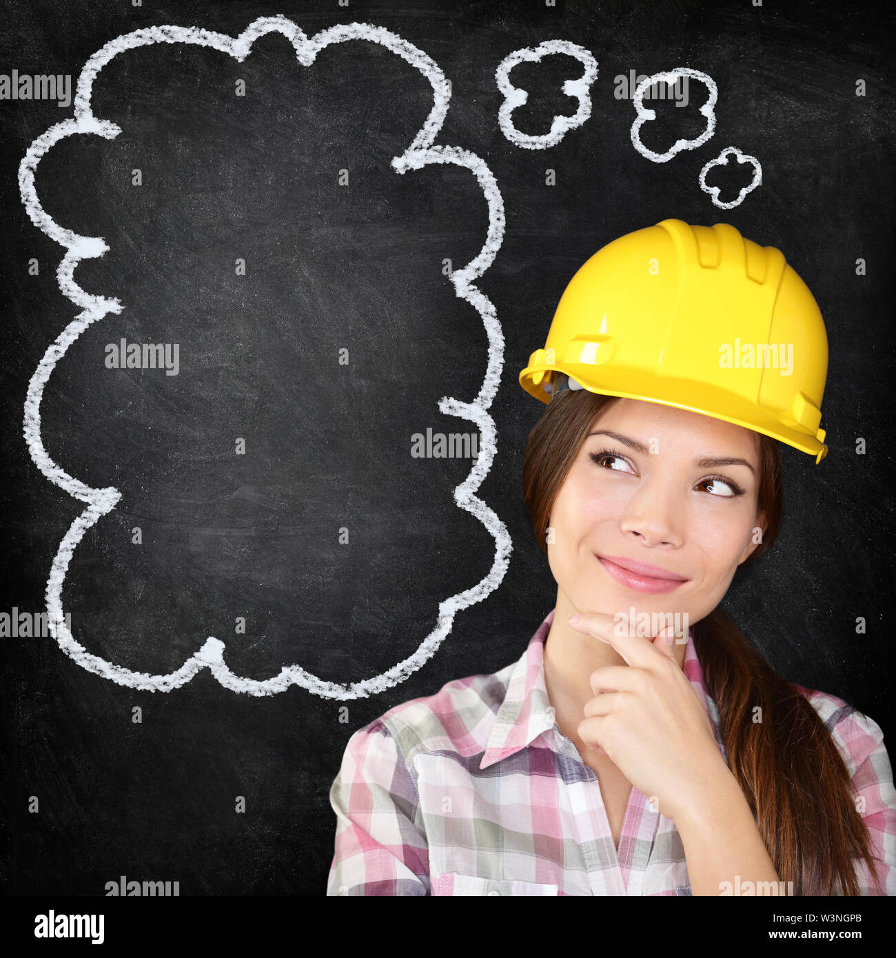 Thinking young female construction worker, architect, engineer, surveyor wearing hardhat on blackboard thinking with hand to chin looking to the thinking bubble on chalkboard texture. Stock Photo
