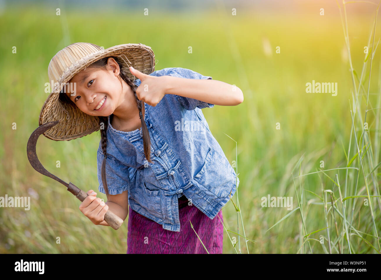portrait of little smiling girl farmer holding sickle on green field Stock Photo
