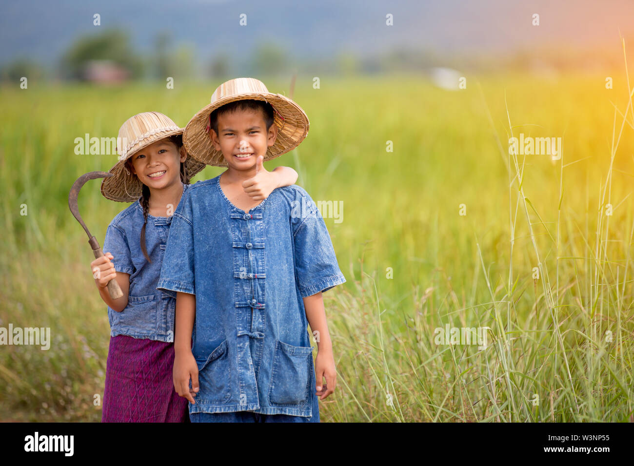 portrait of little smiling young farmer holding sickle on green field Stock Photo