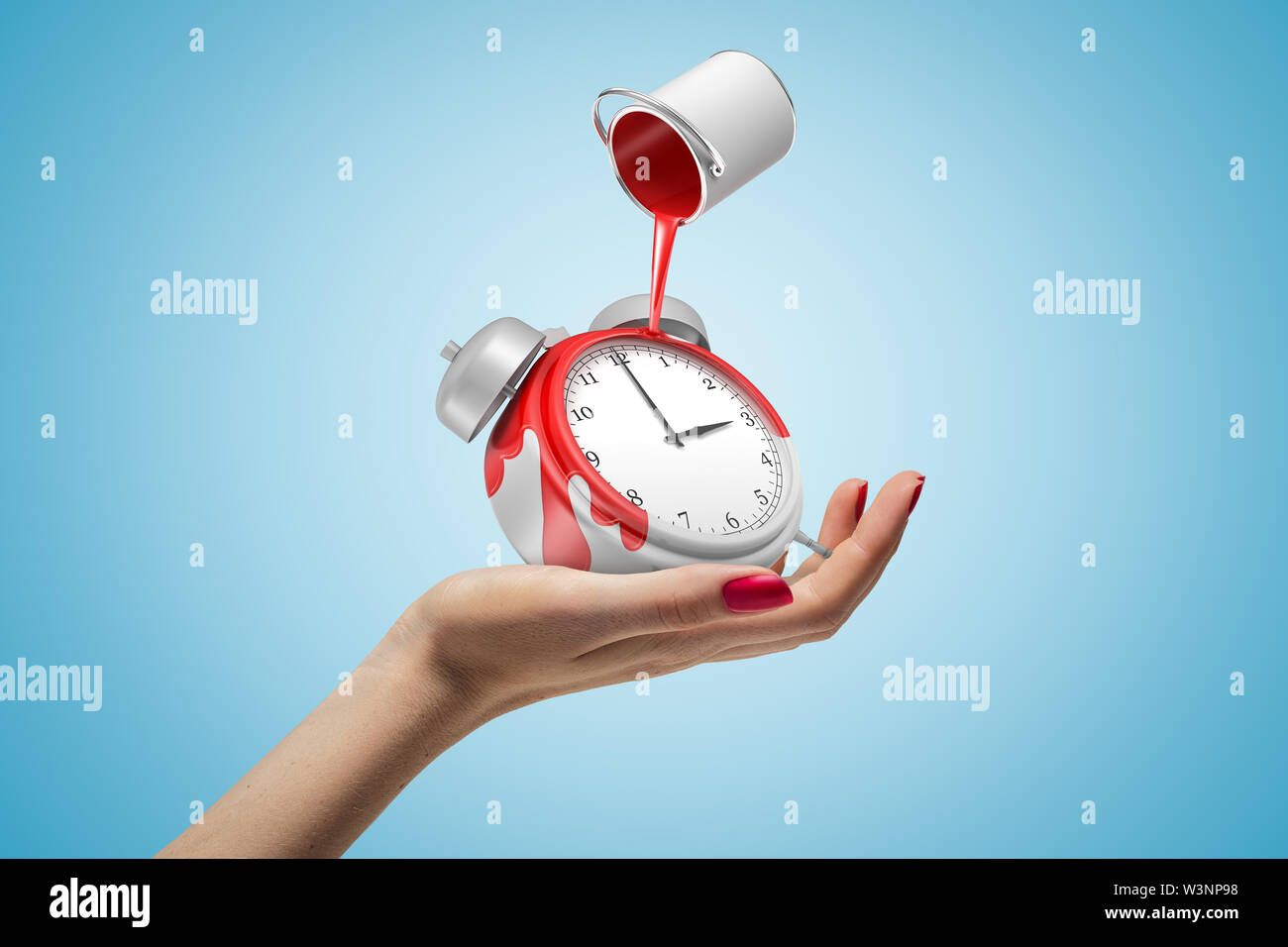 Female hand holding alarm clock with red paint bucket turned upside down above it on blue background Stock Photo