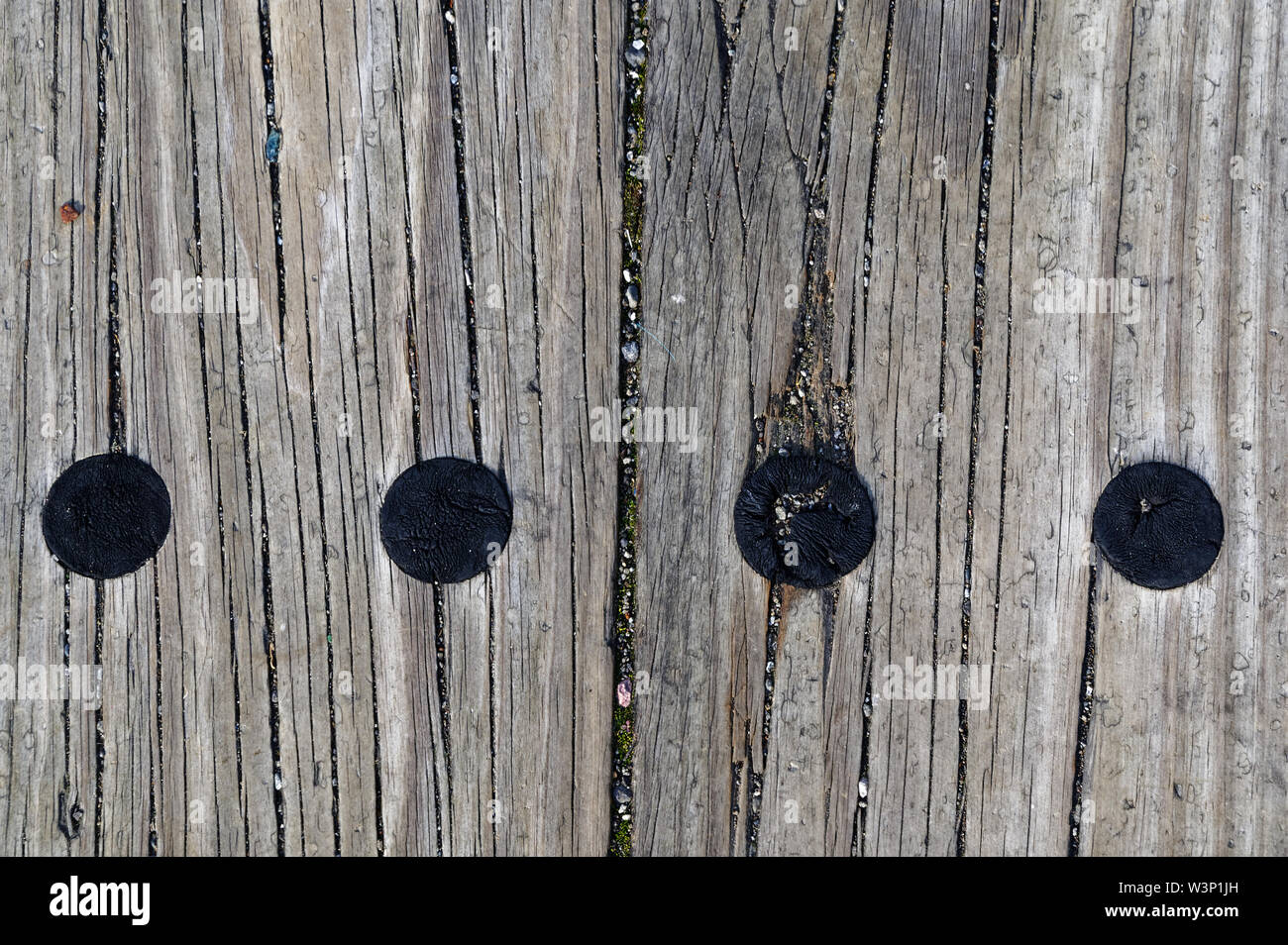 Aged wooden sleepers are on the ground, they have fine gravel in their grooves, there are circular burn marks on them. Stock Photo