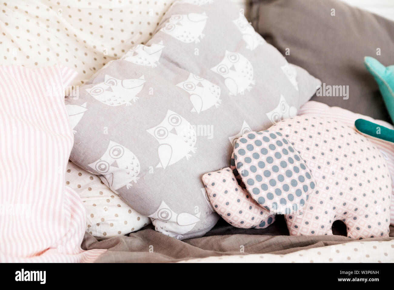Soft baby pillows on the bed. Pillow with painted owls and soft toy in the form of an elephant Stock Photo