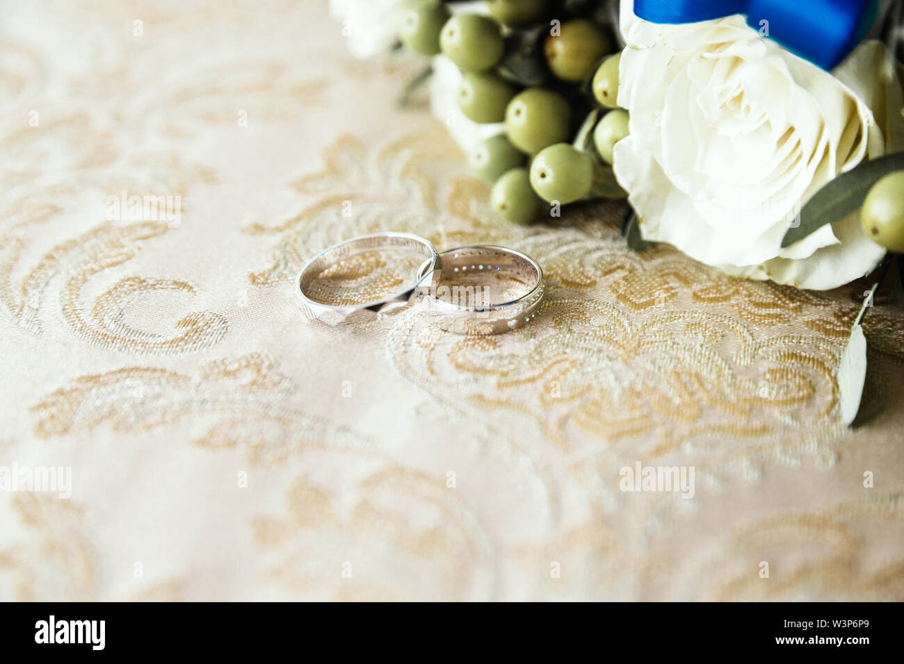 wedding rings lie on the fabric next to a bunch of flowers Stock Photo