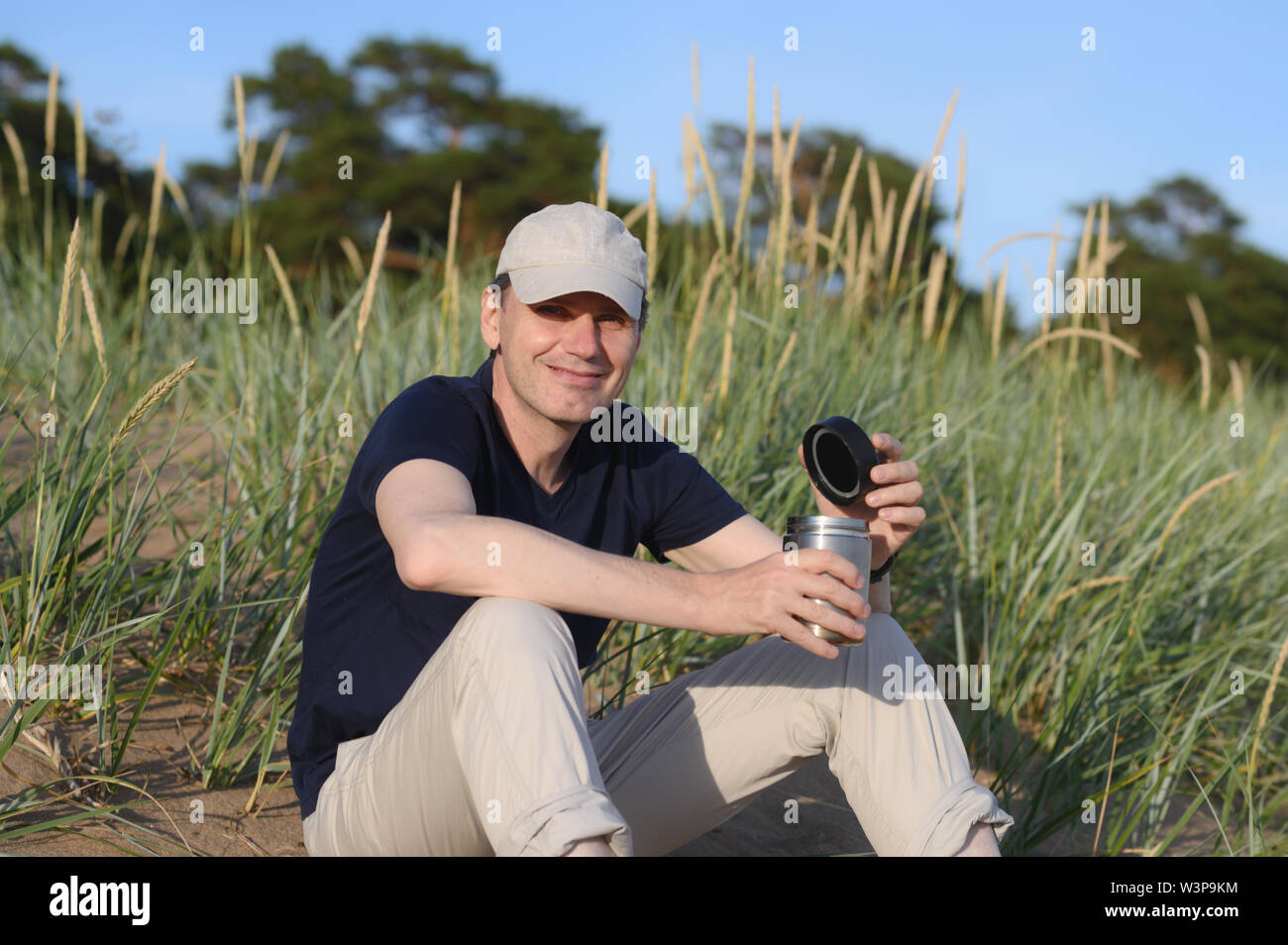 Happy man sitting on a sand dune with a travel coffee mug Stock Photo