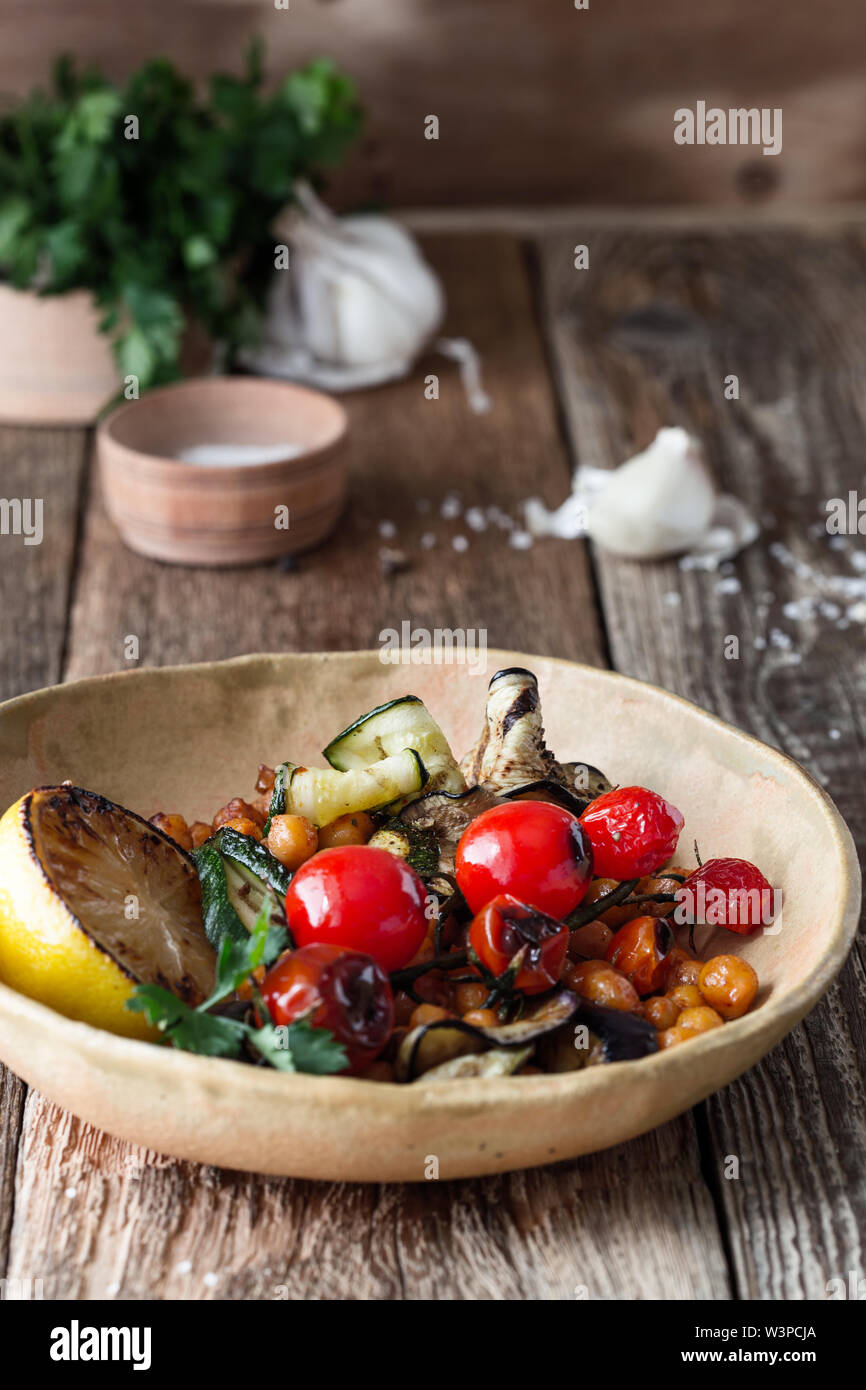 Healthy vegan bowl. Veggie salad with grilled vegetables cherry tomatoes, eggplant, zucchini, crispy crunchy roasted chickpeas in rural ceramic bowl o Stock Photo