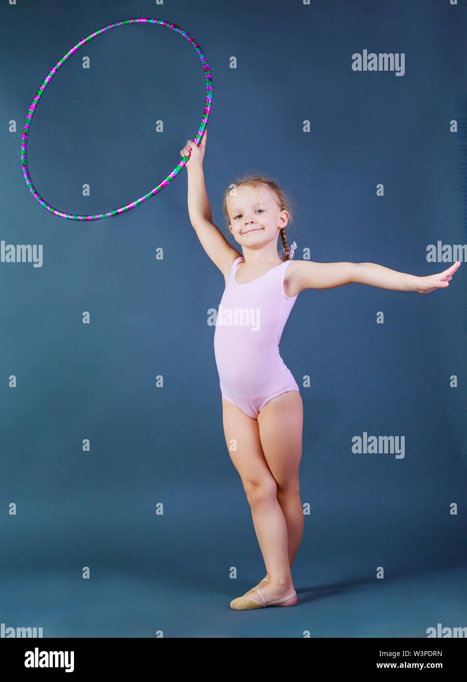 cute girl gymnast with a hoop isolated against blue studio background ...