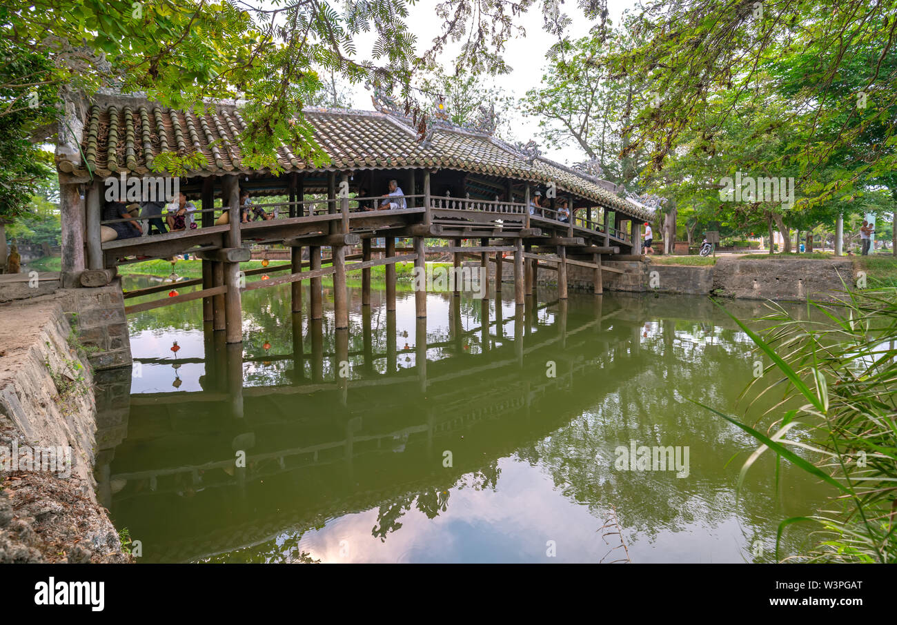 Old wooden bridge crosses the river branch decorated with an upper tile roof dating from the 19th century near Hue city, Vietnam. Stock Photo