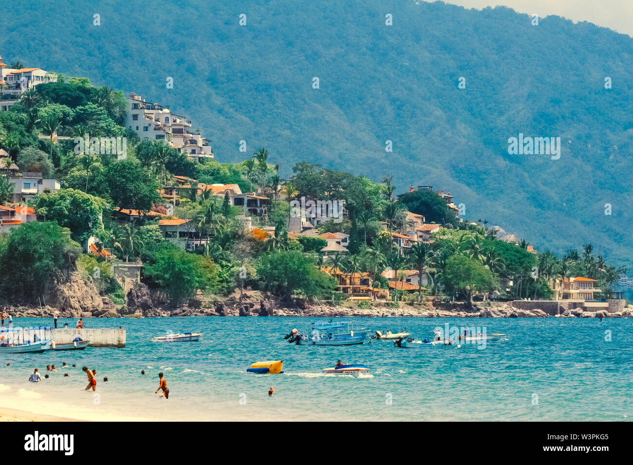 Puerto Vallarta / Mexico - Jun 26.2006: View on the coast beach and turquoise color sea with people swimming and relaxing on the sand. Sunny. Stock Photo