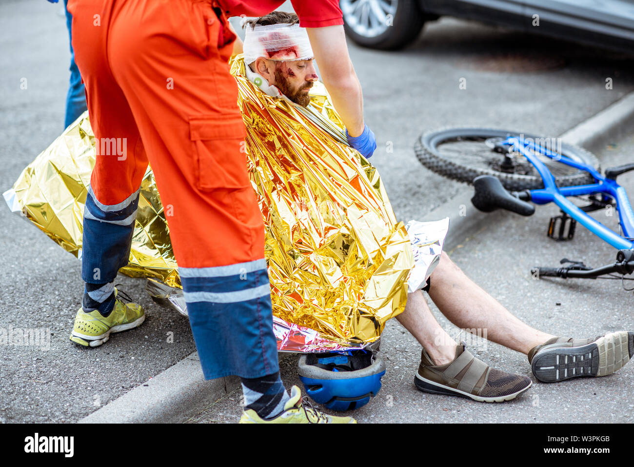 Ambluence worker covering injured man with thermal blanket, providing