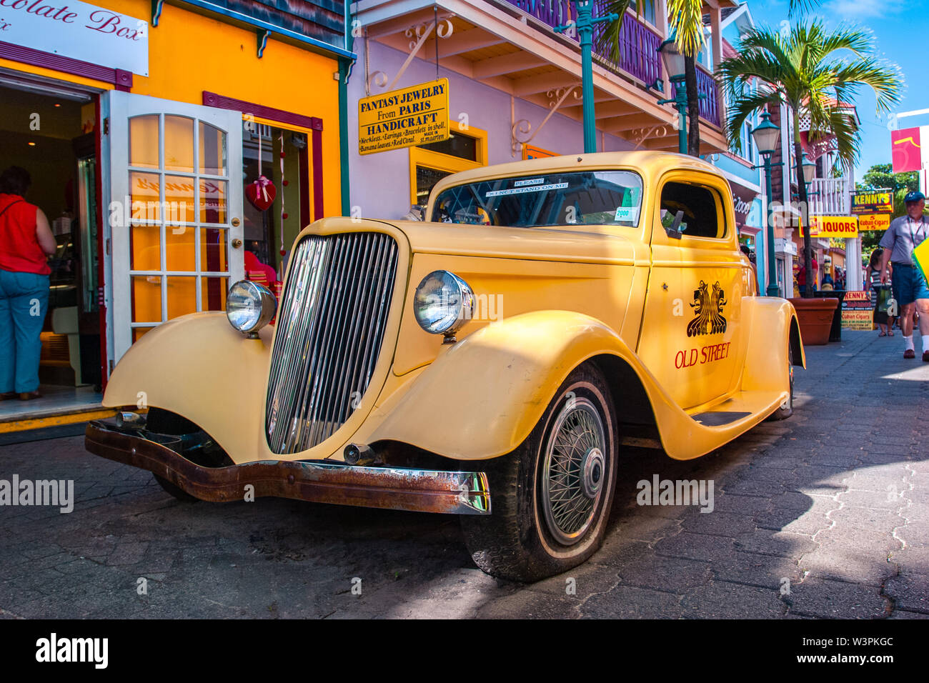 Sint Maarten / Caribbean / Netherlands - January 23.2008: View on the yellow vintage car parked on the street with colorful buildings and palm trees. Stock Photo