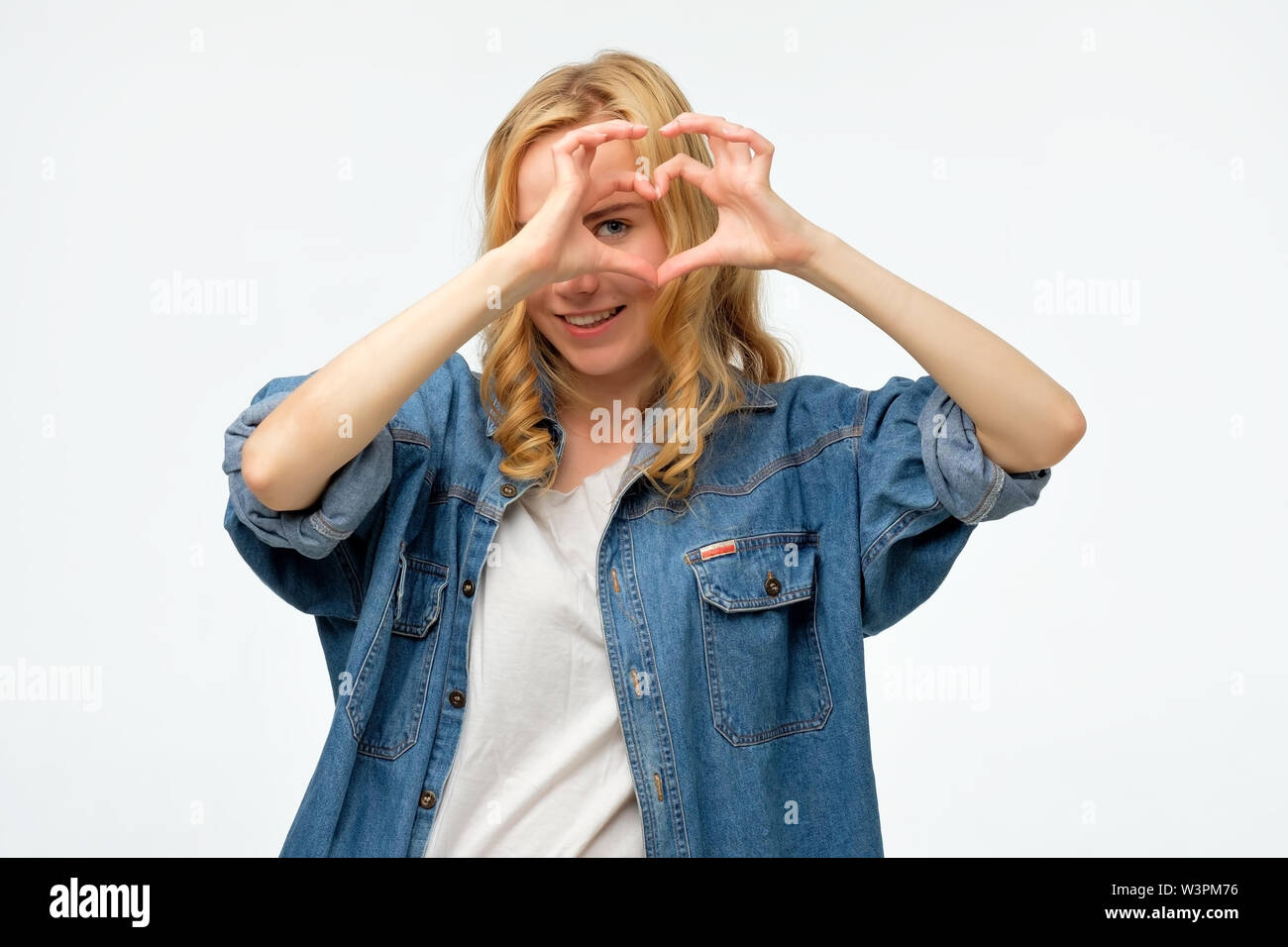 blonde woman smiling in love showing heart symbol and shape with hands ...