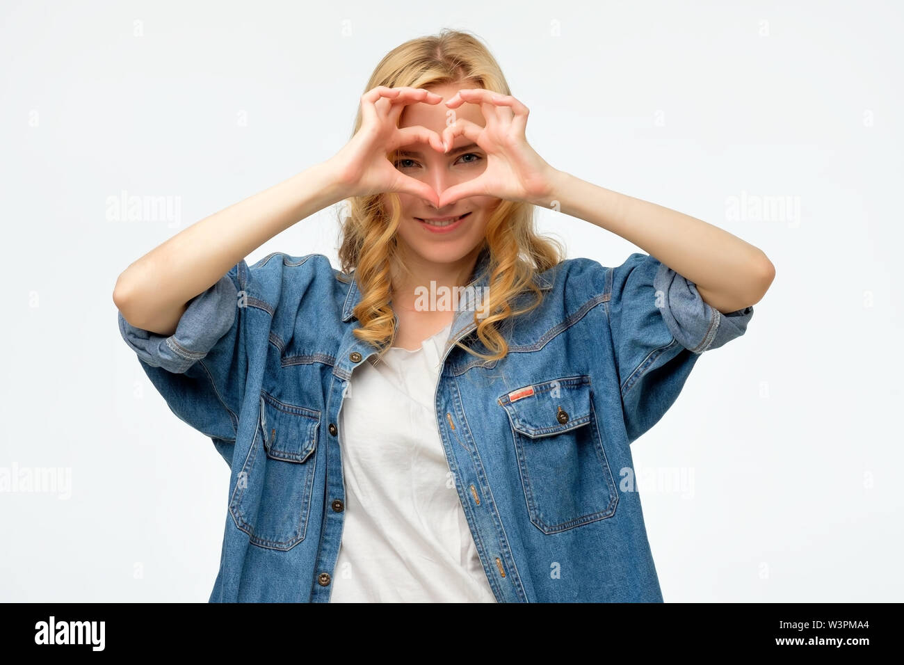 blonde woman smiling in love showing heart symbol and shape with hands ...