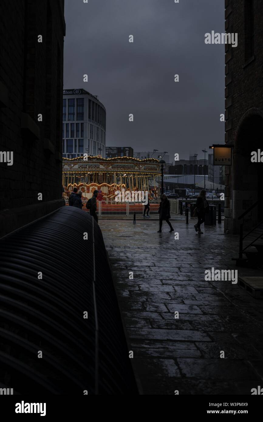 Vertical shot of groups of people walking around carousels during a rainy cloudy day in the city Stock Photo