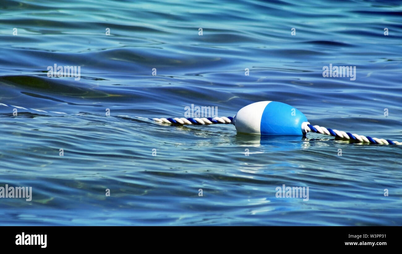 Buoy with attached rope floating on water surface of calm blue lake Stock Photo