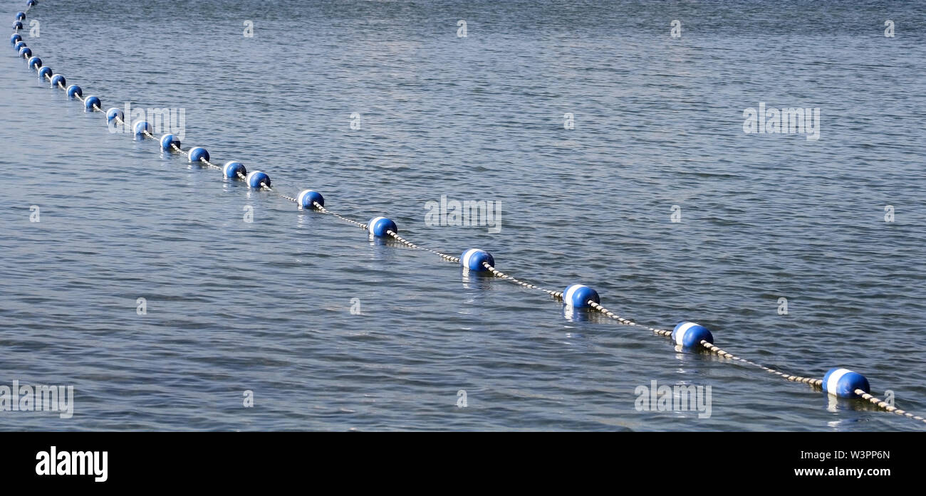 String of blue and white buoys on calm lake waters.  Used as boundary markers to restrict swimming area Stock Photo