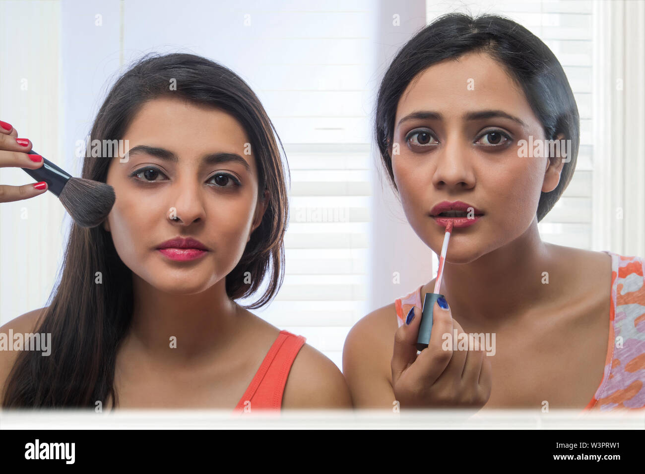 Close up of two teenage girls doing makeup looking into the mirror applying lip paint and brush Stock Photo