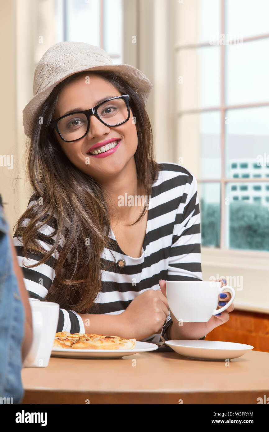 Smiling teenage girl wearing spectacles and hat sitting at restaurant