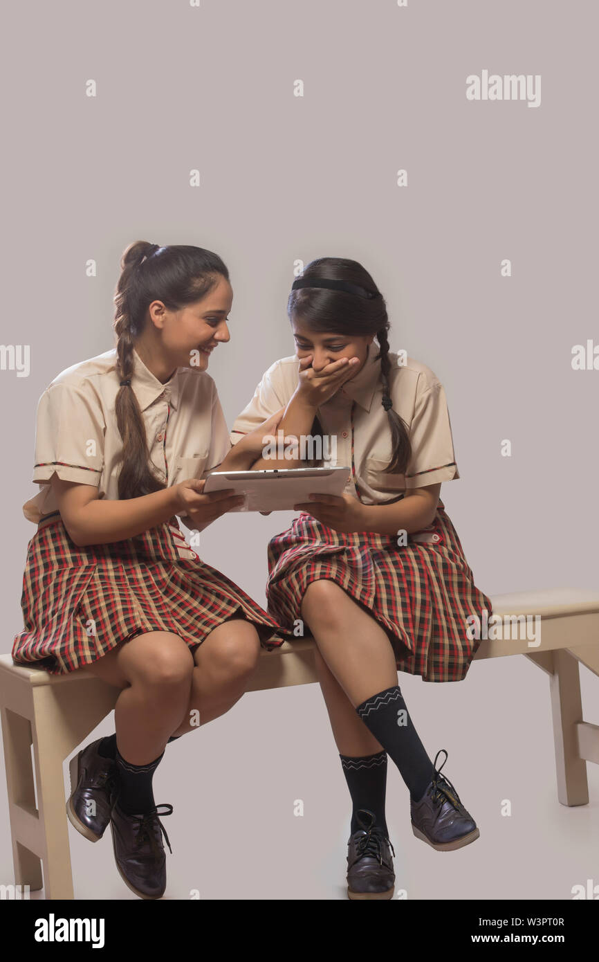 Two girls in school classroom laughing while studying from a digital tablet. Stock Photo