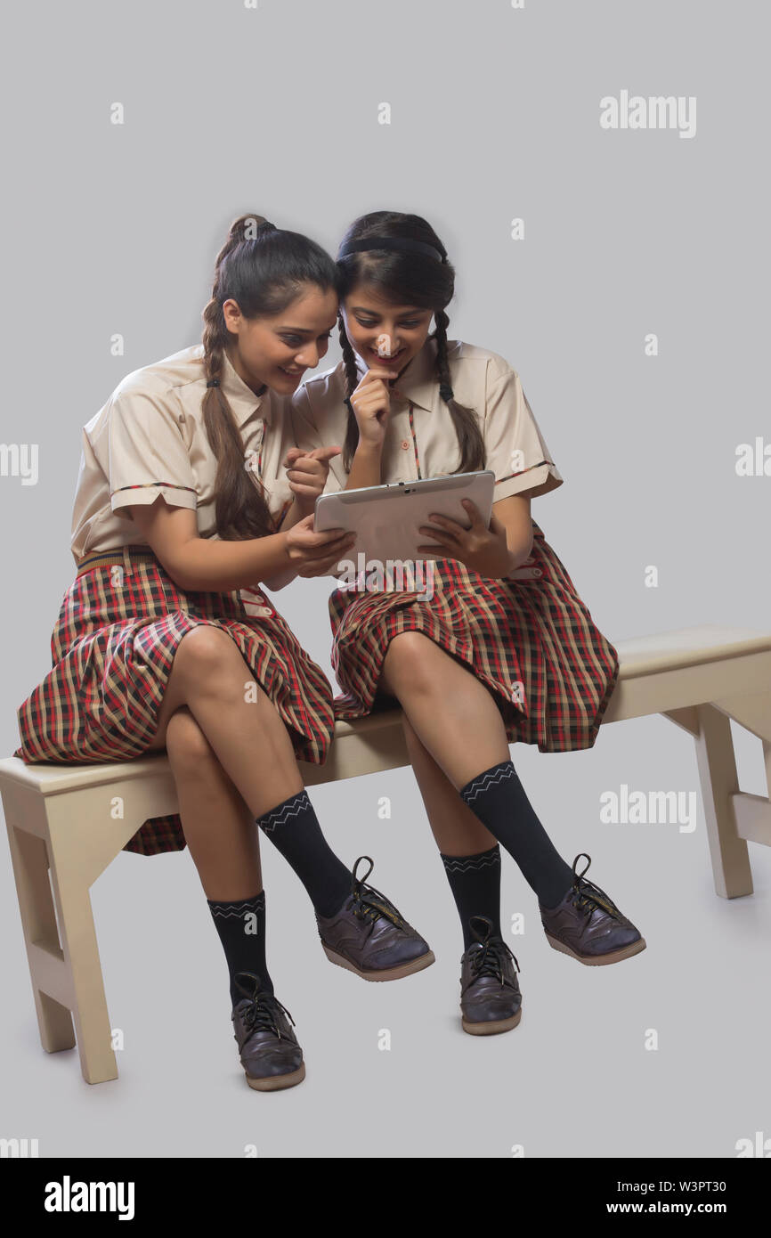 Two girls in school classroom smiling while studying from a digital tablet. Stock Photo