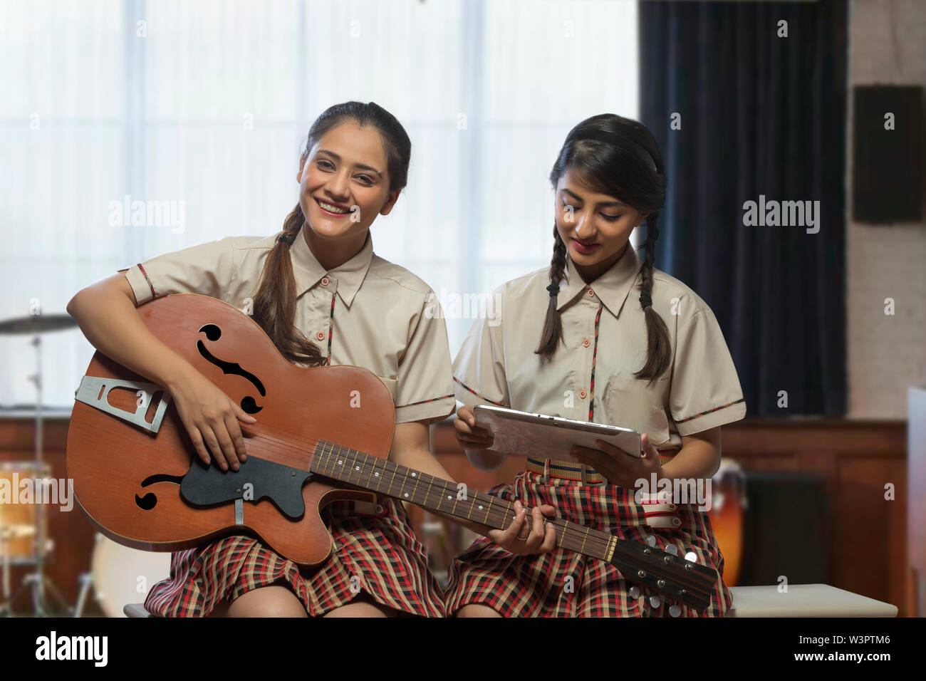 Two happy teenage school girls learning to play guitar in the music room at school Stock Photo