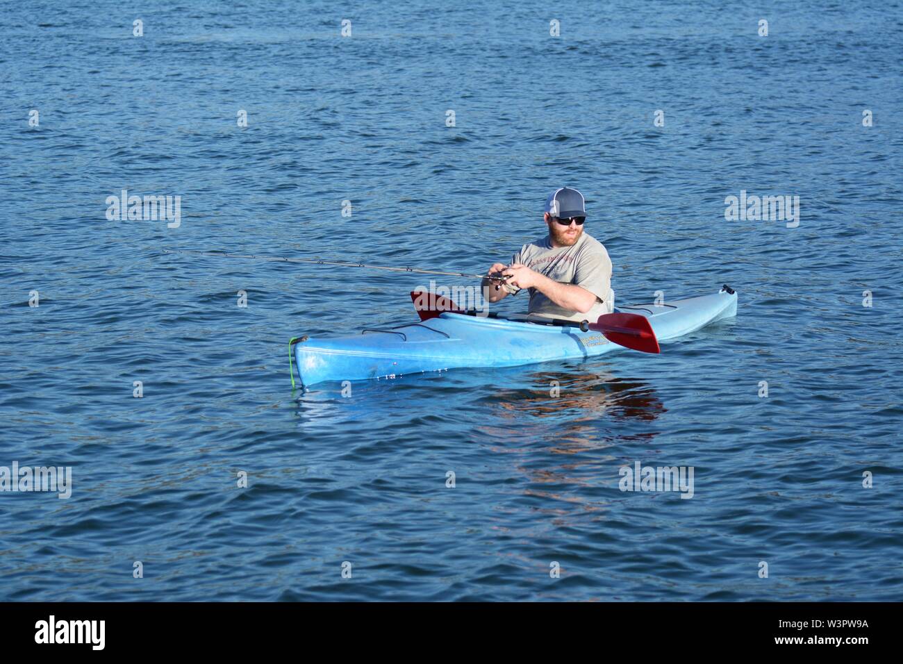 A real happy fisherman with caught small bass on his blue kayak on Clear Lake Clearlake California USA America on calm sunny day in summer by himself Stock Photo