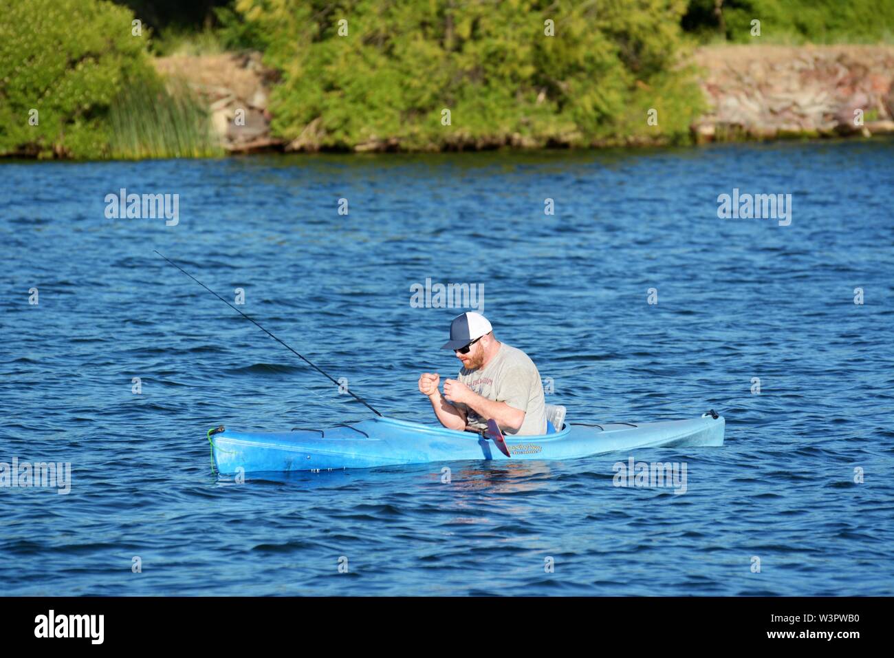 A real happy fisherman with caught small bass on his blue kayak on Clear Lake Clearlake California USA America on calm sunny day in summer by himself Stock Photo