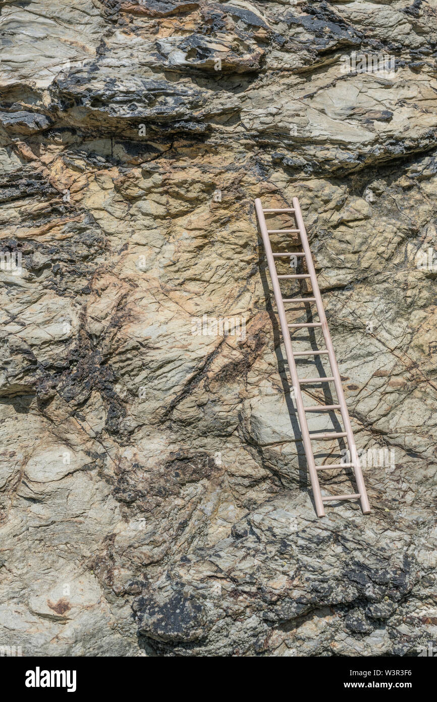 Small wood toy ladder propped against cliff face. Metaphor climbing