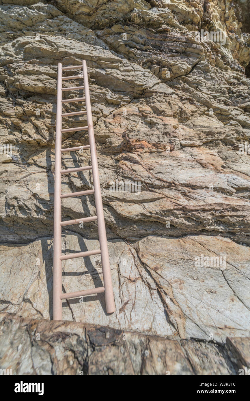 Small wood toy ladder propped against cliff face. Metaphor climbing