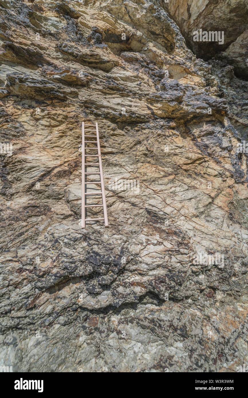 Small wood toy ladder propped against cliff face. Metaphor climbing