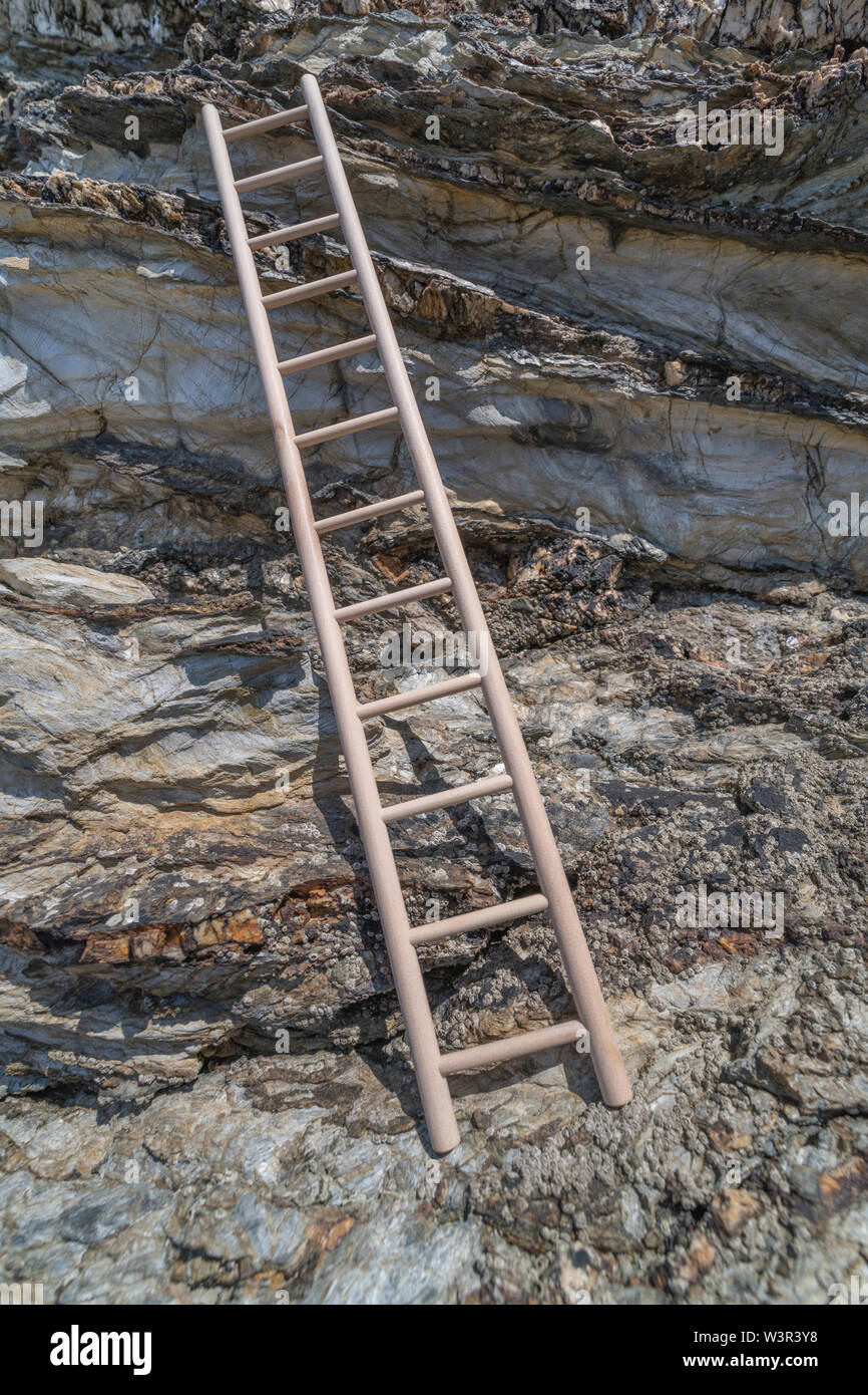 Small wood toy ladder propped against cliff face. Metaphor climbing