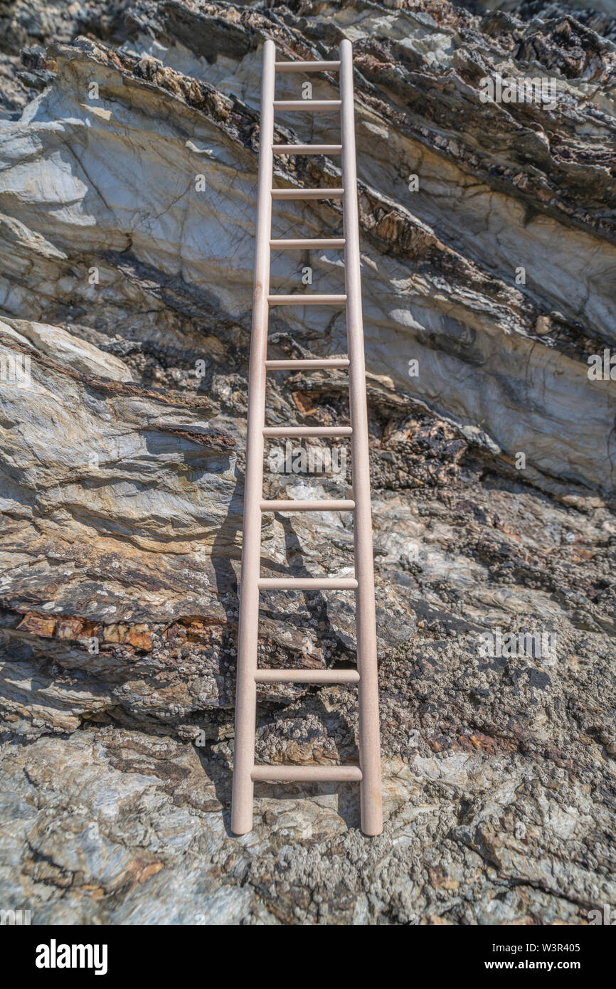 Small wood toy ladder propped against cliff face. Metaphor climbing