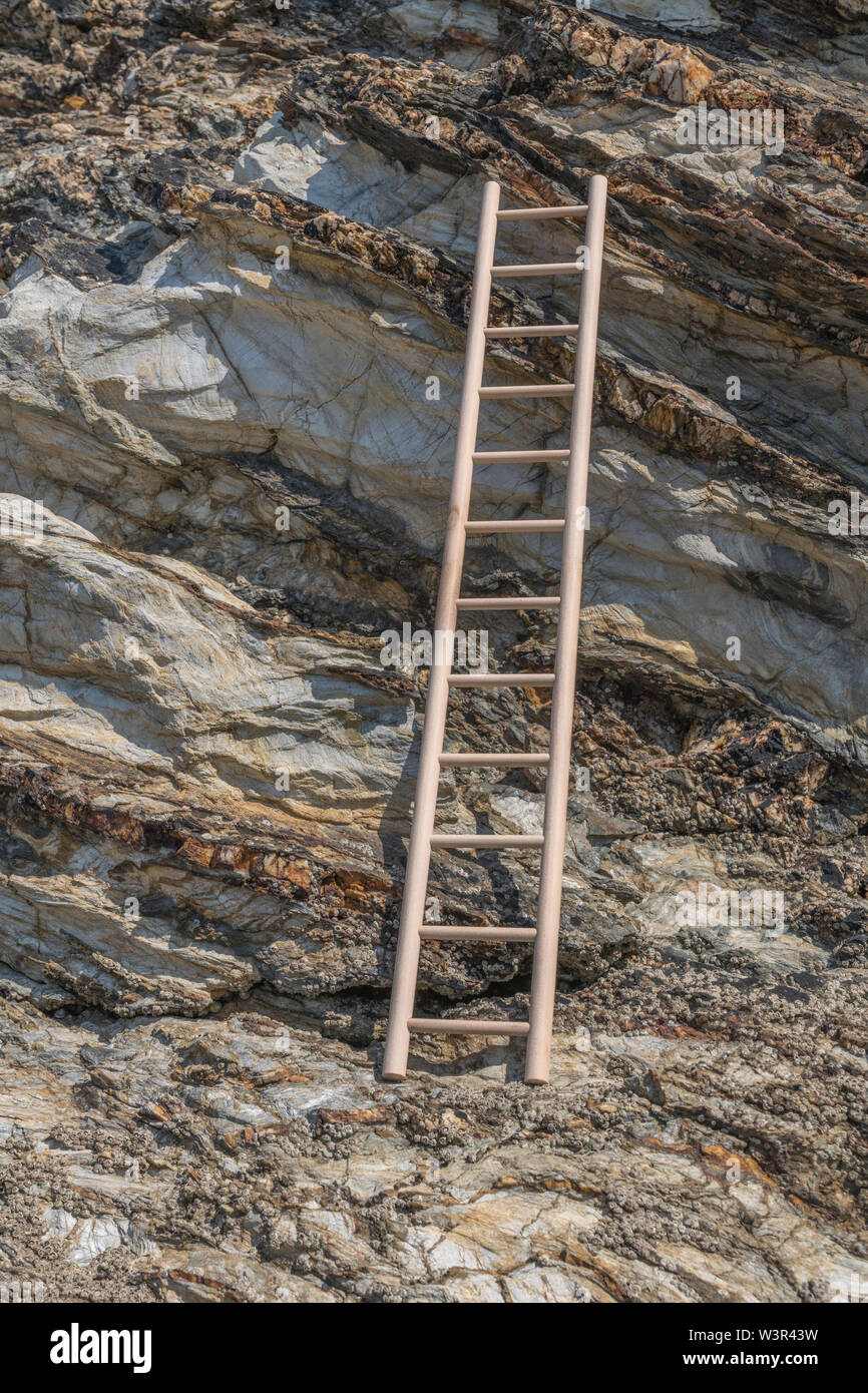 Small wood toy ladder propped against cliff face. Metaphor climbing