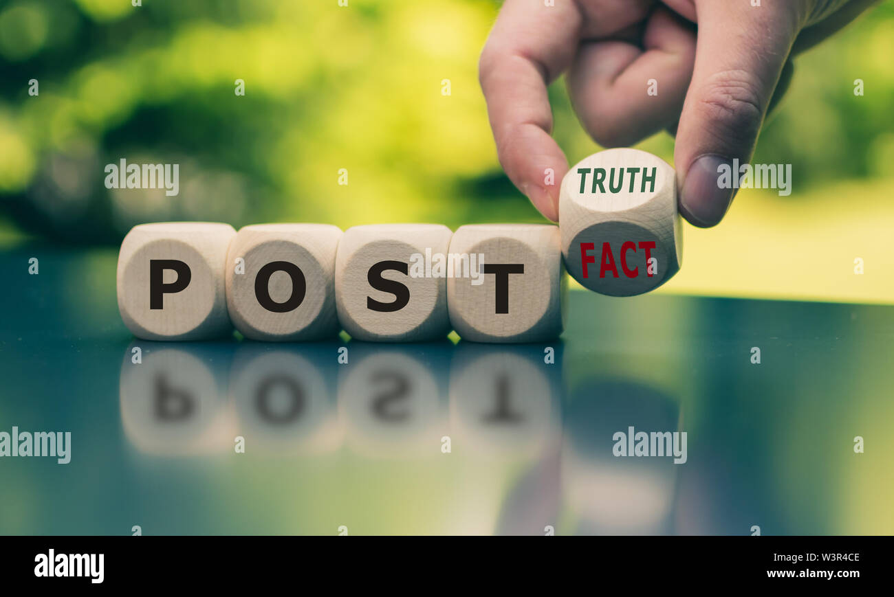 Hand turns a cube and changes the expression 'post fact' to 'post truth'. Stock Photo