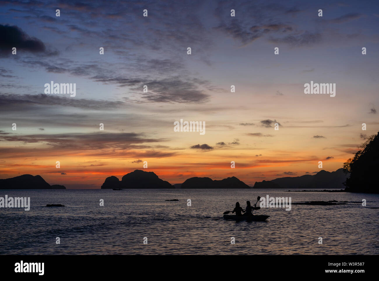 Silhouette of two women paddle in a kayak on the sea along the rocks at sunset, Las Cabanas Beach, Philippines Stock Photo