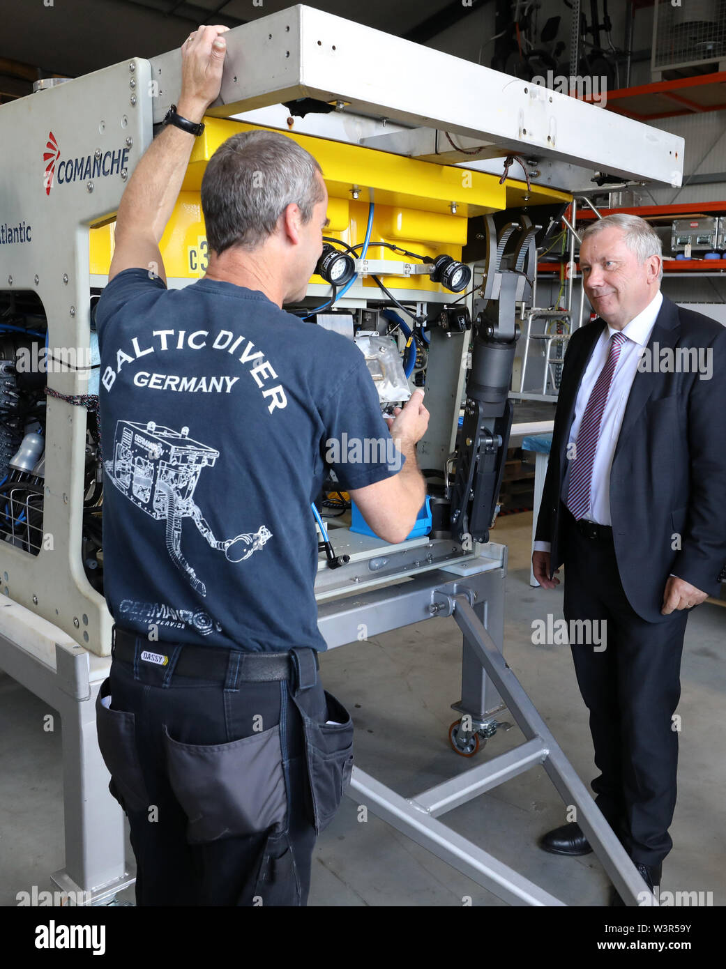 17 July 2019, Mecklenburg-Western Pomerania, Rostock: Andrew Gray (l), Superintendent from Scotland, informs Norbert Brackmann (CDU), coordinator of the federal government for the maritime economy, about the functions of a diving robot during his visit to Baltic Taucherei- und Bergungsbetrieb Rostock GmbH. Brackmann informs himself in the fishing port about the planning status of the 'Ocean Technology Center' (OTC). The OTC is to deal with energy production, raw material extraction or the extraction of food in the sea, among other things, and research the corresponding underwater technology. P Stock Photo